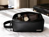 Necessaire Piel Negro abierto en cuarto de hotel con cologne reloj y cartera - viaje ejecutivo MenCity